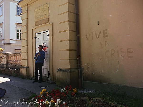A kastély külső fala mellett muzsikáló koldus, és a francia felirat a falon: Éljen a válság!